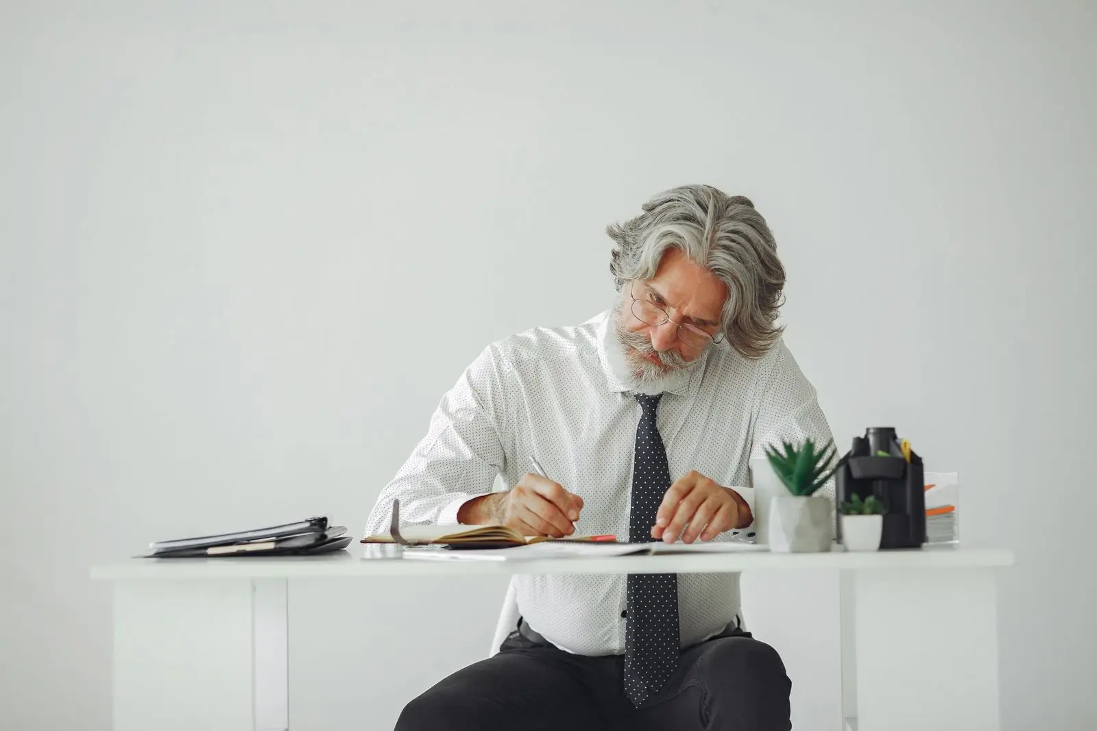 Gray-haired executive writing at a desk in a bright office