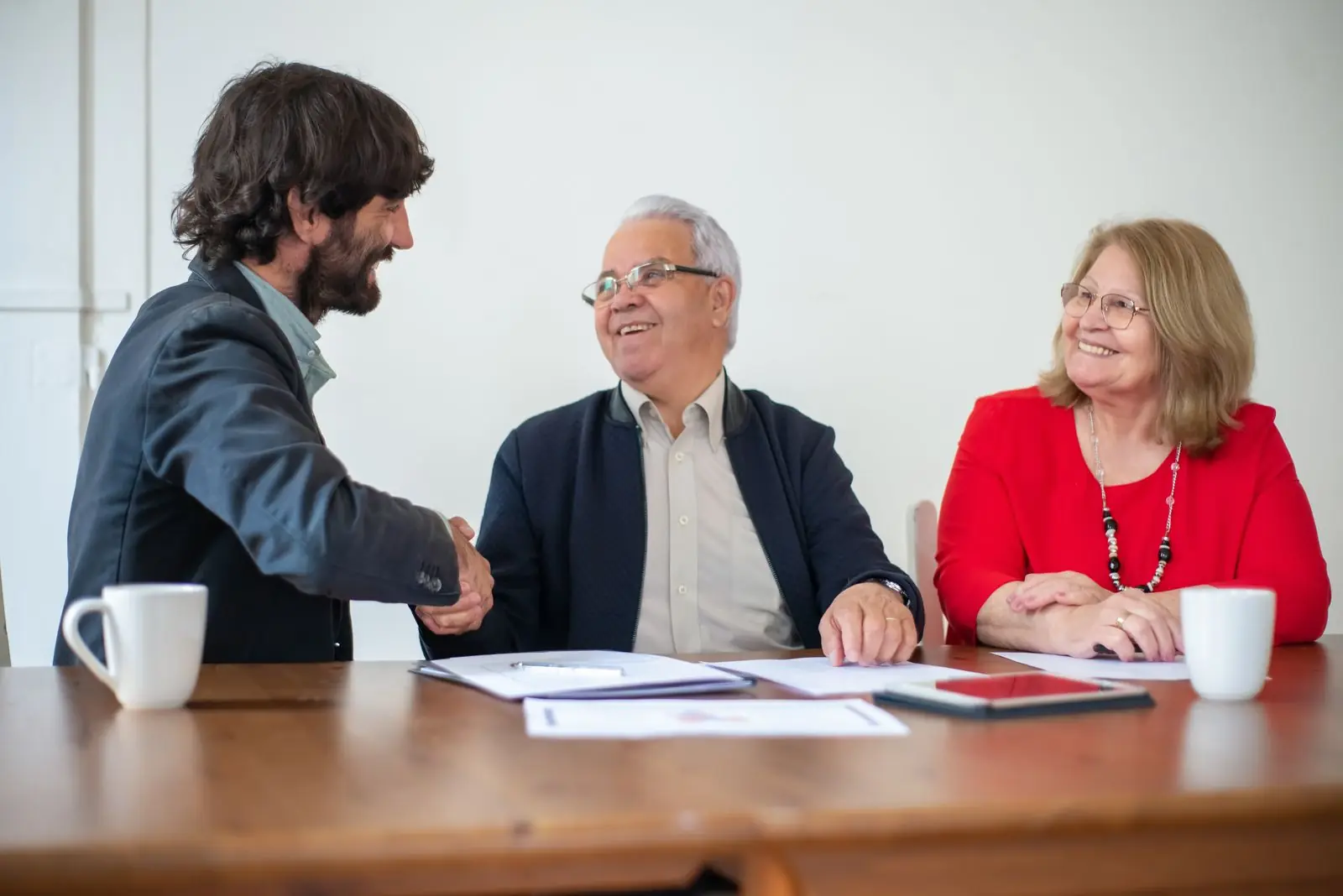 Older and younger professionals shaking hands across a meeting table