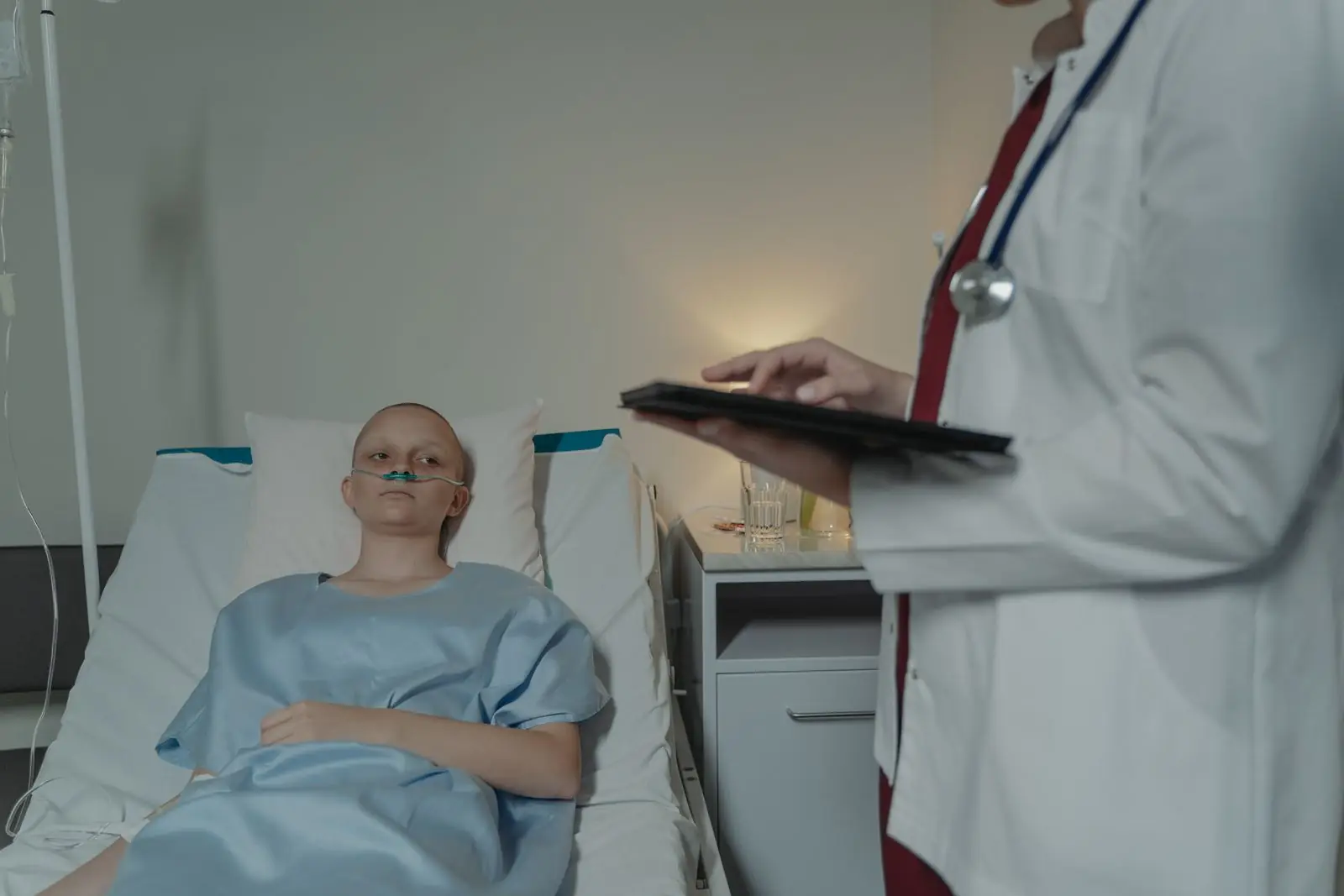 Patient resting in a hospital bed while a doctor checks a tablet